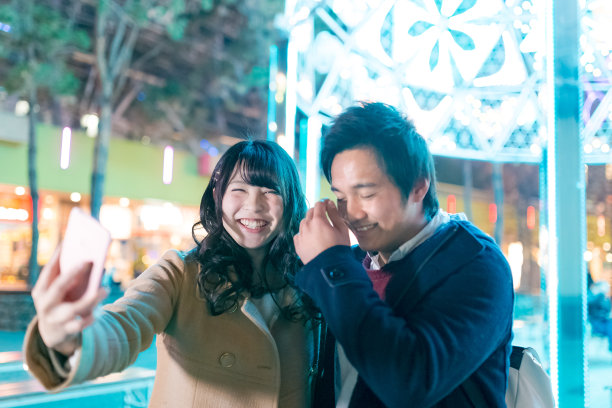 快乐的高中情侣在圣诞彩灯前自拍图片下载