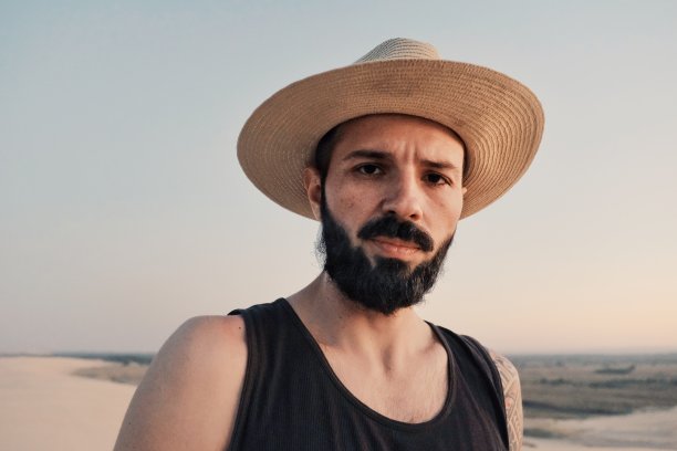 一个年轻人戴着草帽在城市旁边的一个小沙漠地区的沙丘上探险图片下载