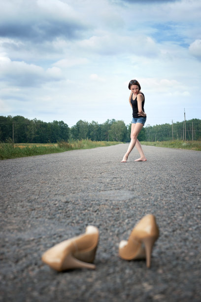 年轻的女孩光着脚走在路上，她把鞋子丢在路上，忘记了夏天和旅行的概念图片下载