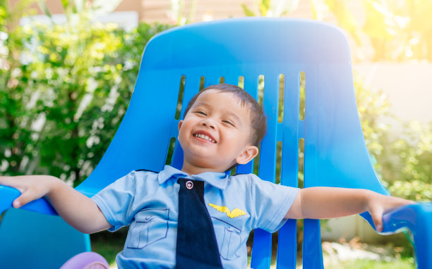 亚洲幼儿园男孩骄傲地坐在蓝色的椅子上，穿着飞行员的制服。以微笑、快乐为教育理念。图片下载