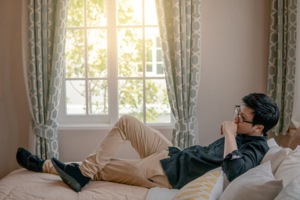 年轻的亚洲幸福的男人与眼镜躺在舒适的床上在舒适的复古卧室。居家城市生活方式概念图片下载