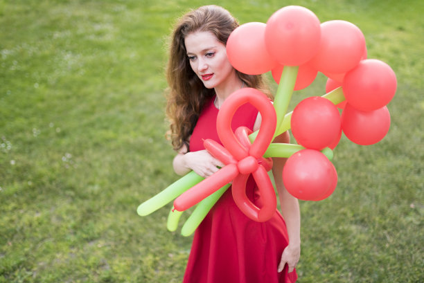 一个孤独的女人穿着红色衣服，在公园里捧着气球图片下载