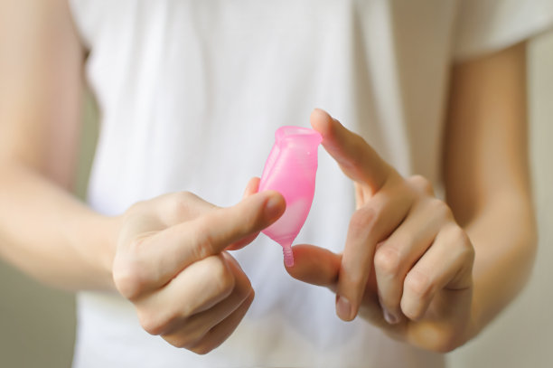 年轻女子手持经期杯。妇科概念，循序渐进的指导，如何使用月经杯。选择性聚焦，水平靠近模糊的背景。jpg图片下载