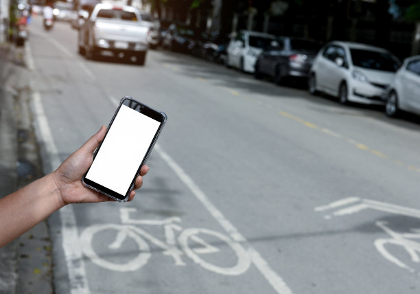 手持智能手机白色显示屏，模糊的道路背景。图片下载