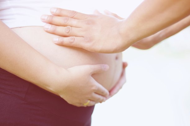 丈夫抱着怀孕的妻子的肚子。新妈妈，穿着白色内衣的孕妇。年轻女子等着生孩子站在户外。图片下载