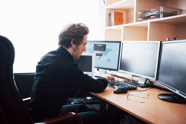 这个年轻危险的黑客通过下载敏感数据和激活病毒来破坏政府服务。一个男人使用一台有很多显示器的笔记本电脑图片下载