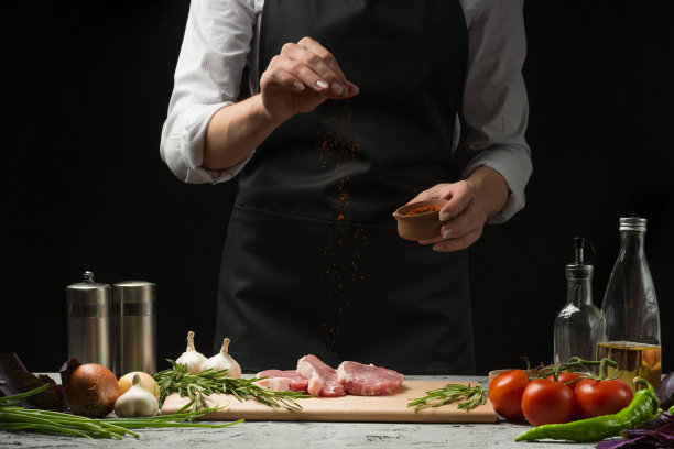 厨师烧烤牛排。新鲜牛肉或猪肉的制备。撒上红辣椒或红辣椒。水平照片与深黑色背景。图片下载