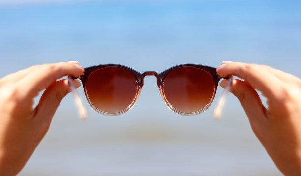 在蓝色的大海和太阳的背景下，双手握着女人的太阳镜图片下载