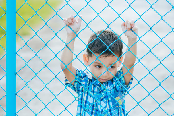 那个男孩站在篱笆后面。图片下载