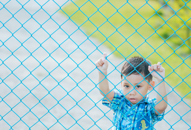 那个男孩站在篱笆后面。图片下载