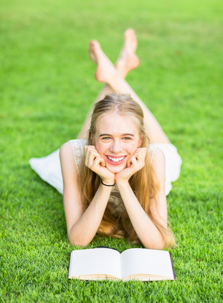 快乐的年轻女孩在草地上阅读图片下载