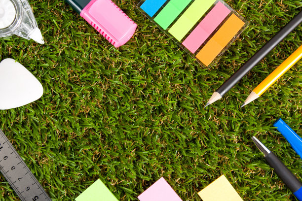 钢笔、铅笔、橡皮、马克笔、修正带和贴纸躺在绿色的人造草地上。前视图。图片下载
