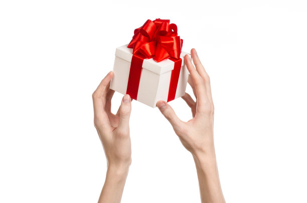 庆祝和礼物的主题:手拿一份包裹在白色盒子里的礼物，上面有红色的丝带和蝴蝶结，这是工作室里最美丽的礼物图片下载