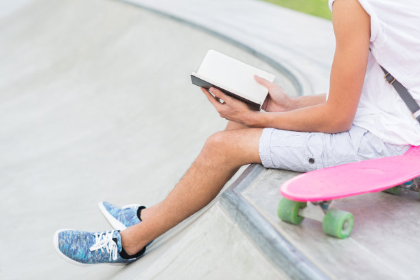 年轻男子在滑板公园阅读的特写镜头图片下载