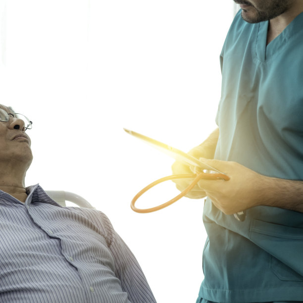 老人躺在内科病房的帆布床上。医生问他的病情，老医生问老病人问题。图片下载