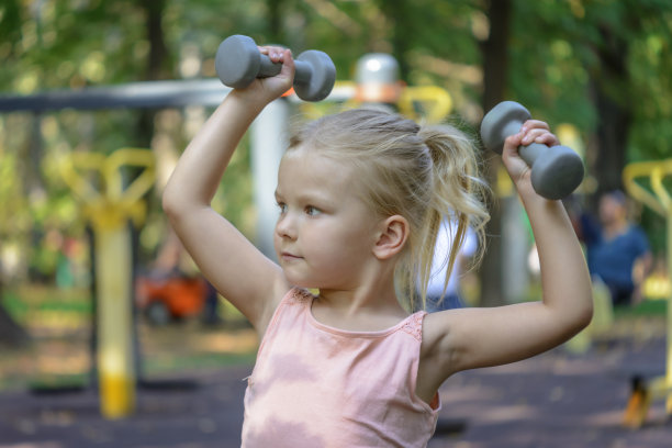 一个金发小女孩喜欢运动。操场上的孩子举起了哑铃。健康的生活方式。图片下载