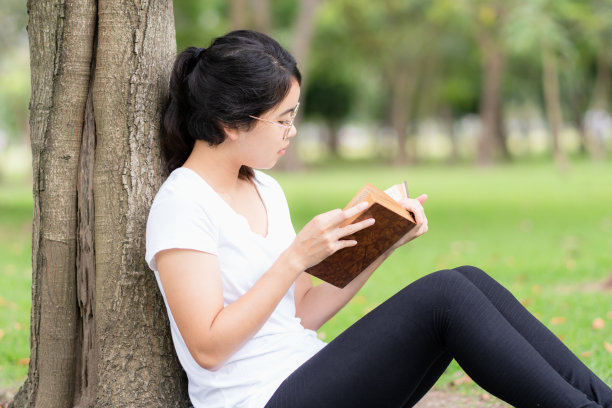 戴眼镜的年轻女子在公园里读旧书。图片下载