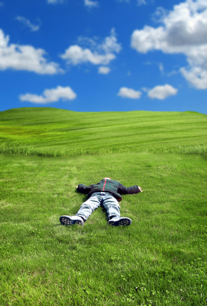 小男孩躺在碧绿的草地上，天空晴朗图片下载