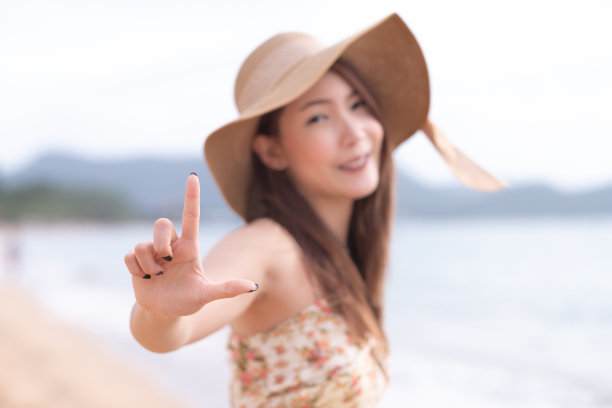 在海滩上，一名年轻的亚洲女子用手举着“L”的符号，暗示着“爱”图片下载