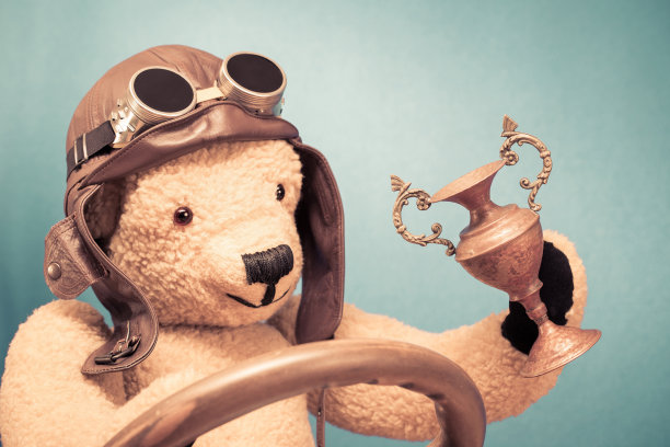 复古泰迪熊玩具在皮革飞行员的帽子和复古眼镜与获奖者的杯子前薄荷绿墙背景。老式滤镜照片图片下载