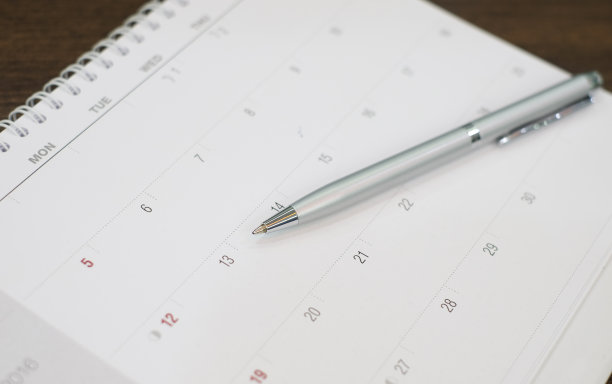 近距离用圆珠笔在日历上准备写日期约工作，会议:办公用品为企业概念素材图片