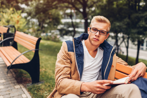 大学生背着书包看书，在秋天的公园里散步，坐在长椅上图片下载