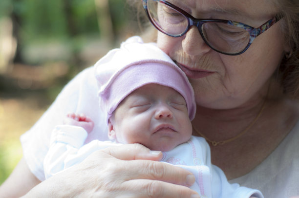 戴眼镜的祖母双手抱着一个戴着粉色帽子的刚出生的小孙女。图片下载