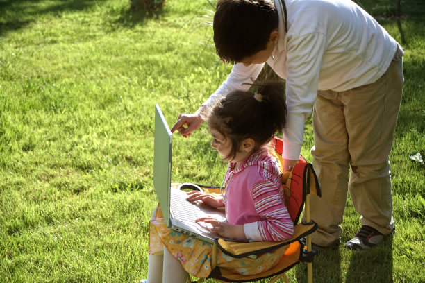 小女孩和小男孩用手提电脑在绿草如茵的草地上嬉戏图片下载