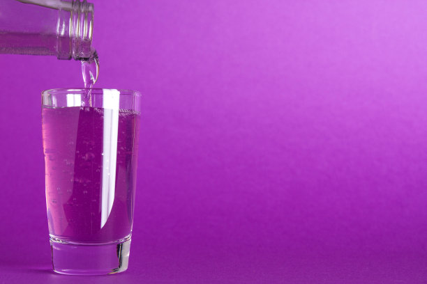 将紫色的碳酸液体从紫色背景的瓶子里倒进玻璃杯图片下载