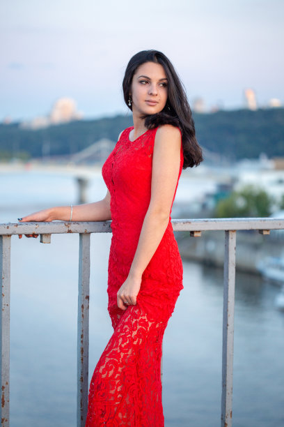 漂亮的年轻女孩穿着红色的裙子在一座老篱笆附近的桥上摆姿势。图片下载