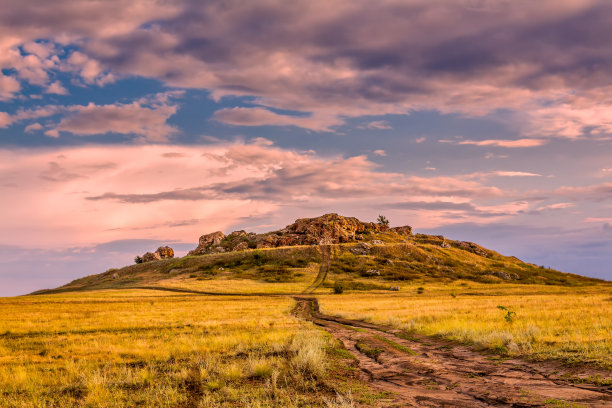 雾蒙蒙的山路延伸到山顶上的夕阳景观。阳光穿过树林。图片下载