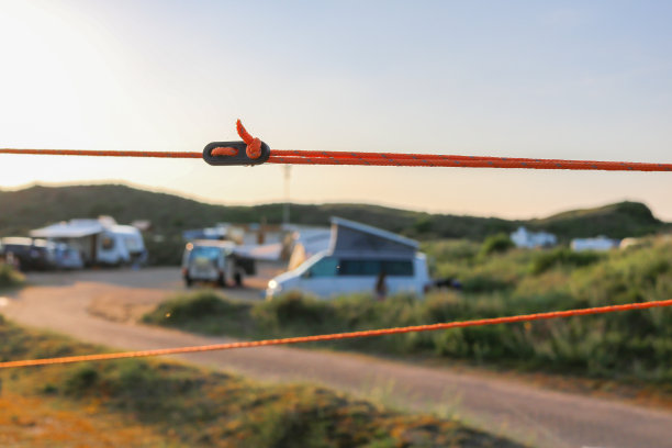 橙色的牵索和黑色的调整器将一个帐篷固定在它的位置。牢固固定与大篷车，露营者和露营场地的背景。图片下载