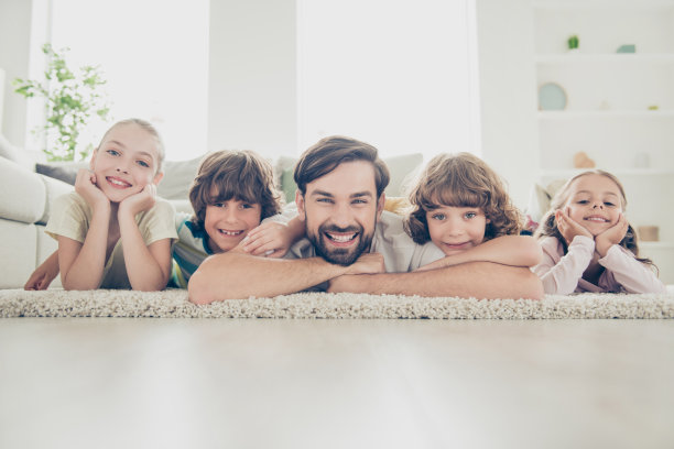 近距离的照片，单身的十多岁的爸爸躺在柔软的地毯地板上，可爱的兄弟姐妹孩子靠近舒适，舒适的沙发或沙发在现代光线室内图片下载