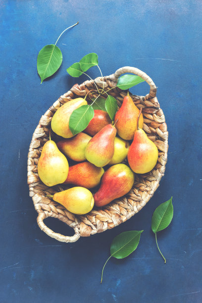 红黄相间的梨子放在篮子里，背景是乡村的蓝色。俯视图，调色照片。图片下载