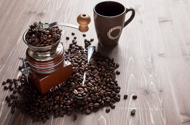 咖啡豆在咖啡研磨机和咖啡杯在棕色的木制背景图片下载