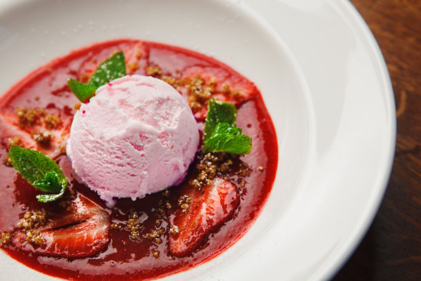 特写照片的粉色冰淇淋勺在盘子与红色的果酱，草莓片和薄荷叶。前视图。图片下载