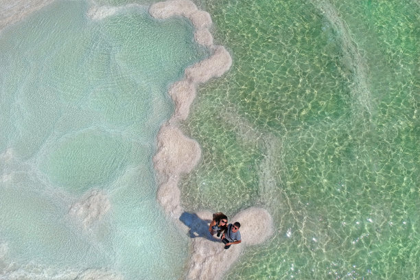 夫妻在眺望，死海蜜月之旅，水中天然盐沉积纹理图片下载
