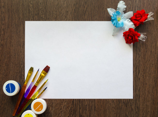 空白白纸为您的文本在一个深色的木桌背景。周围有彩色的颜料、画笔和花。模型图片下载