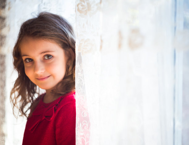 天真快乐的小女孩躲在窗帘后面素材图片