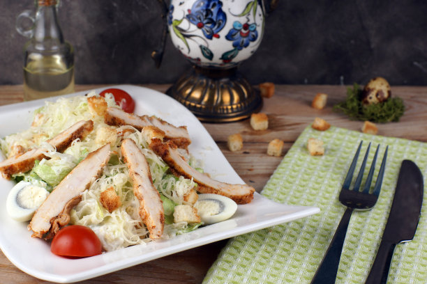 盘子里有鸡肉凯撒沙拉，旁边有绿色的毛巾和餐具图片下载