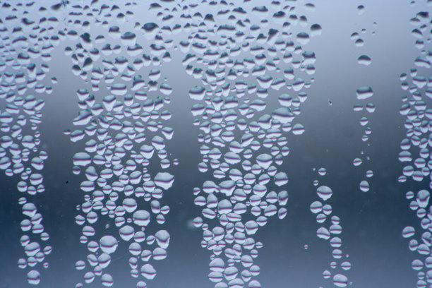 几滴水滴在玻璃杯上。蓝色背景的窗口。图片下载