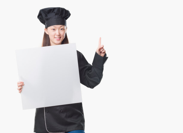 年轻的中国女子在孤立的背景下穿着厨师制服，举着横幅惊讶地提出一个想法或问题，开心地指着手指，第一图片下载