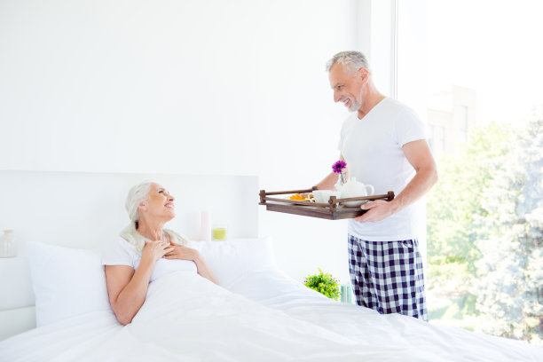 早上浪漫的概念。侧面照片的男人在睡衣带来早午餐在舒适的床上，他的妻子。无忧无虑，无忧无虑，如梦似幻的人们在明亮的白色室内图片下载