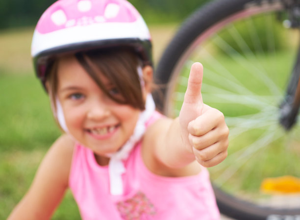 迷人的小自行车手给大拇指。快乐快乐的小女孩与自行车的背景手势向上户外。孩子，积极的情绪和生活方式。图片下载
