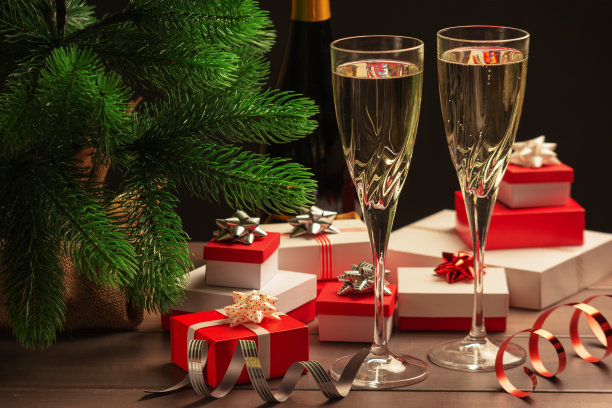 喜庆的圣诞晚会。两杯香槟，许多带蝴蝶结和装饰丝带的礼品盒。美丽的照片在黑暗的背景。图片下载