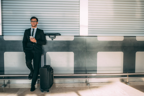 一个年轻的商人拿着箱子站在机场等飞机图片下载