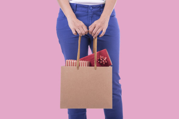 手持购物纸袋和礼品盒在粉红色的背景。圣诞购物和新年快乐的概念。图片下载