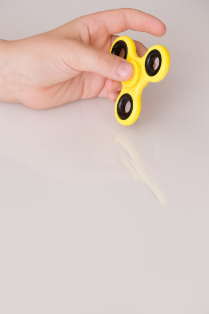 孩子的手旋转指尖陀螺装置。前视图。玩一个黄色的手旋转坐立不安玩具图片下载