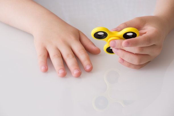 孩子的手旋转指尖陀螺装置。前视图。玩一个黄色的手旋转坐立不安玩具图片下载