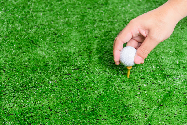 这个男人的手正在把高尔夫球放在球座上。在绿色的草坪上。为高尔夫球比赛做准备。图片下载